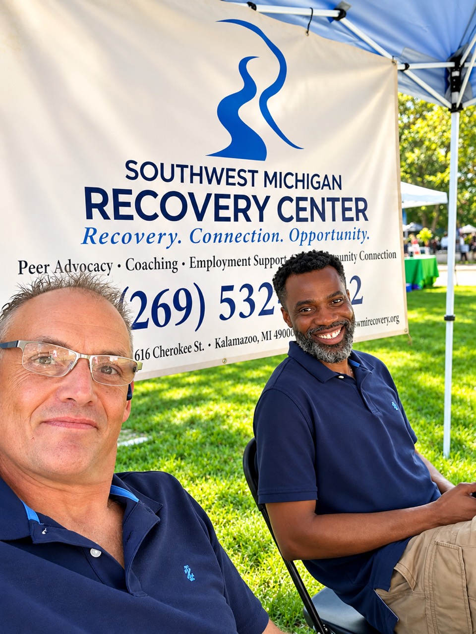 Two people seated beside an SMRC banner at an outdoor booth